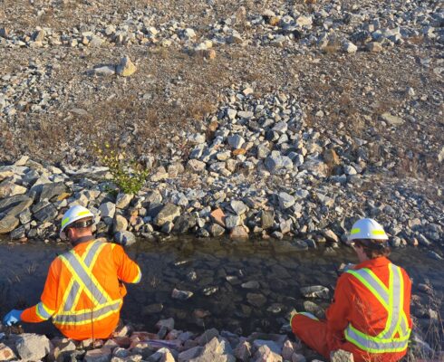 Duncan McDonald, Environmental Scientist, and Mike Bower, Environmental Scientist, wearing Hi-Vis jackets, collecting a water sample from a stream.