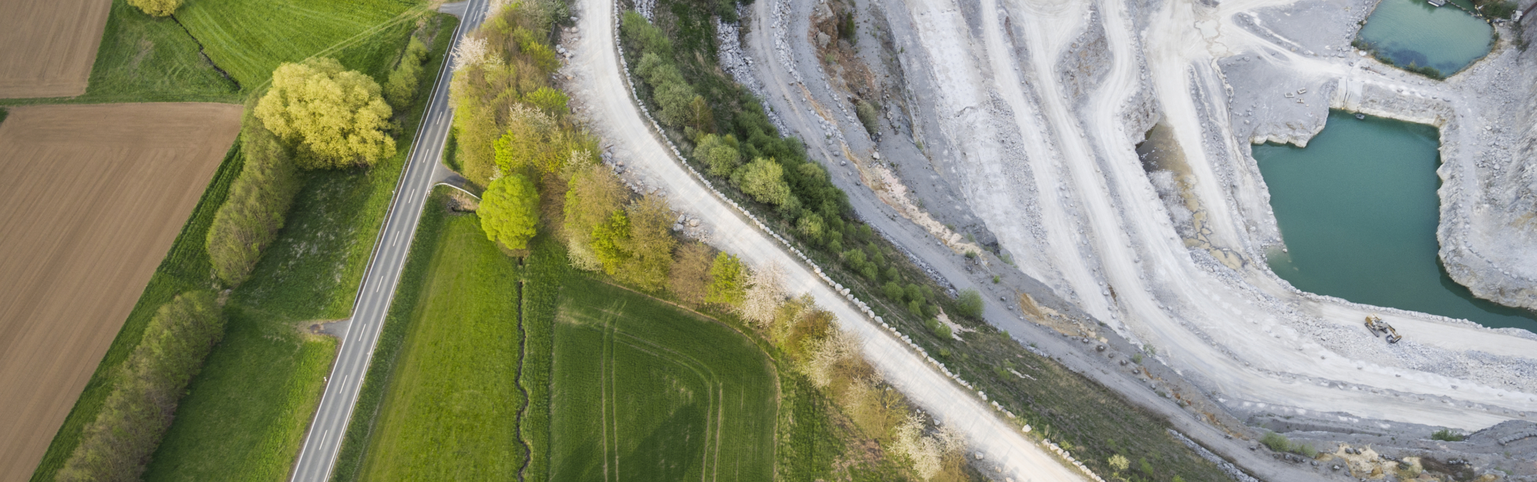 Aerial view of a large limestone quarry, fields, and a road.