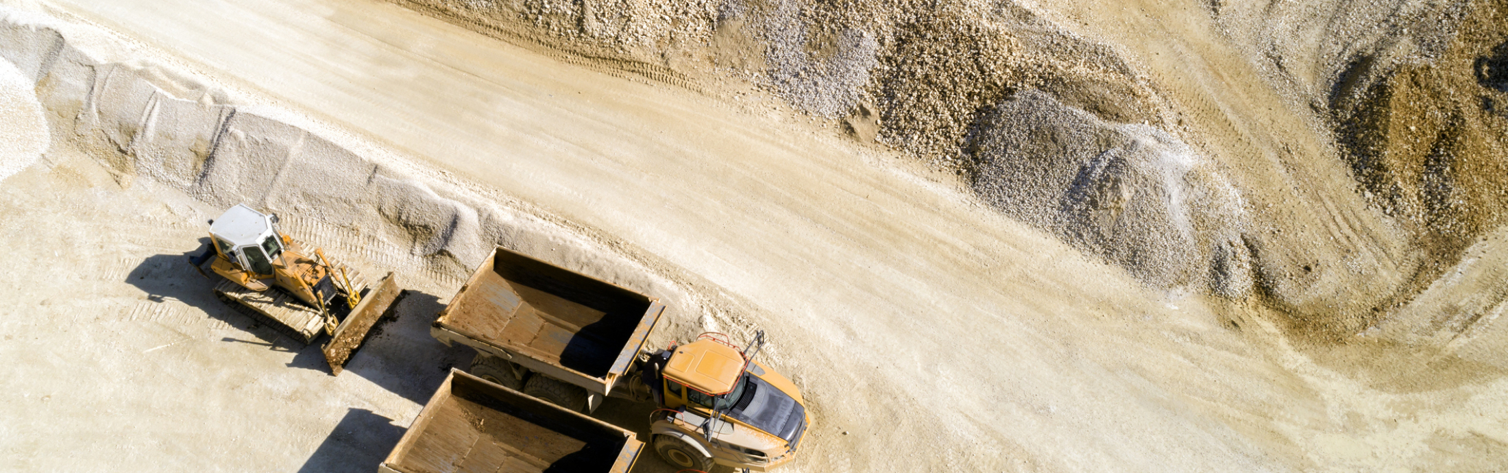 Aerial view of two dump trucks and a bulldozer in a quarry.