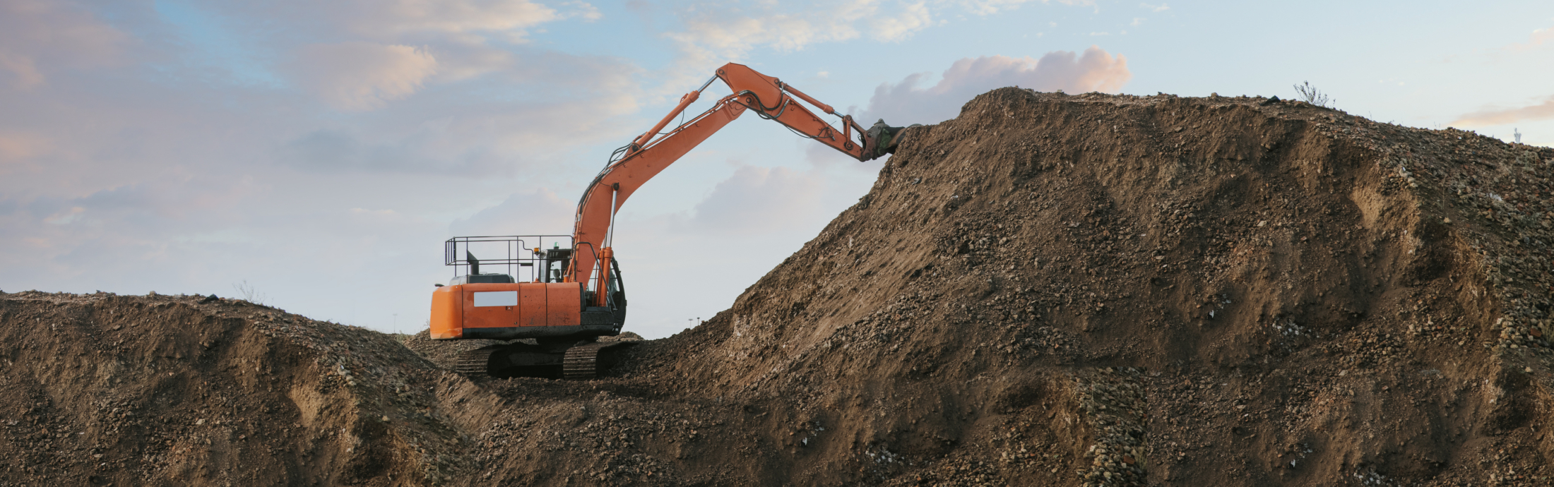 Excavator bulldozer in sandpit with raised bucket over blue cloudscape sky.