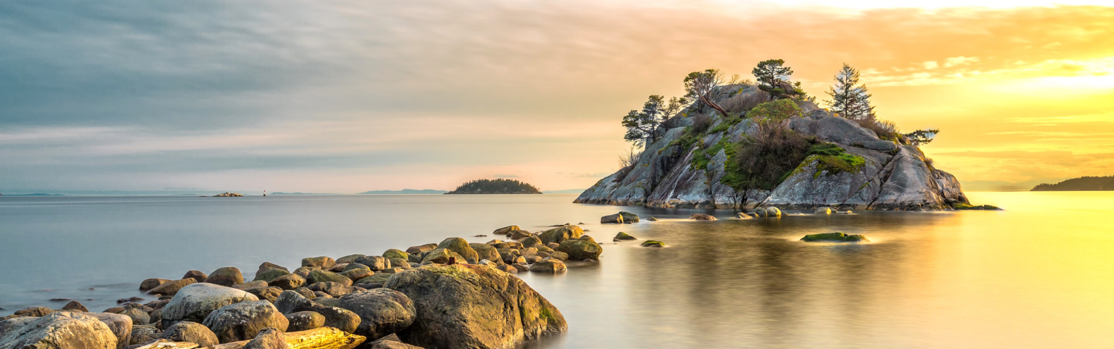 Rocks lead out to still water at sunset.
