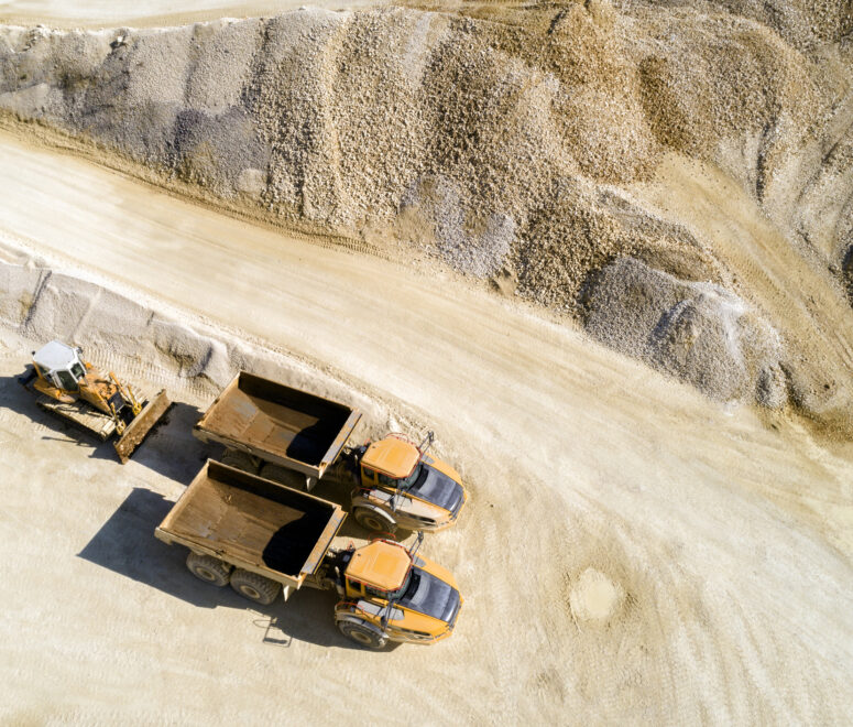 Aerial view of two dump trucks and a bulldozer in a quarry.