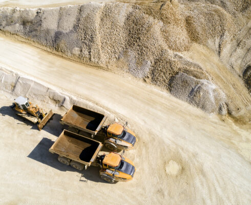 Aerial view of two dump trucks and a bulldozer in a quarry.