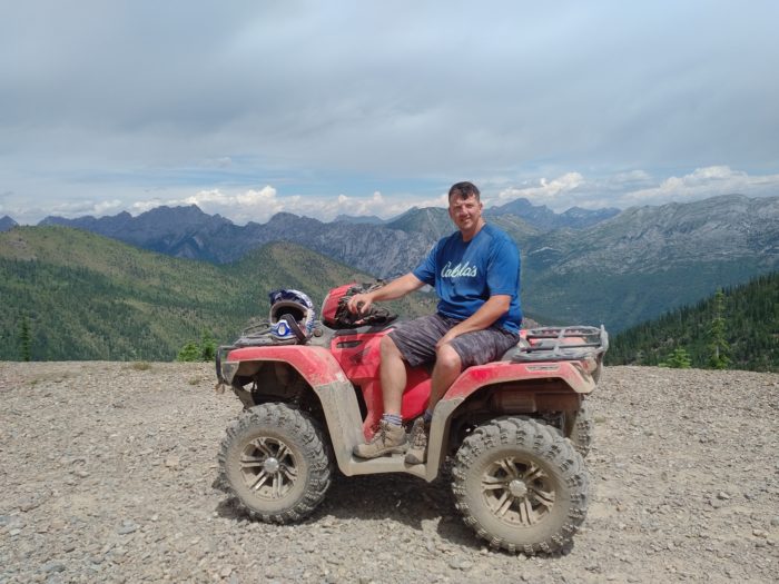 Joe sits on a quad bike with a mountain range behind him.