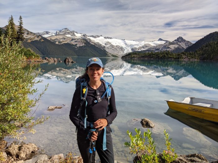 Mackenzie Bromstad standing in front of a lake with mountains in the distance.